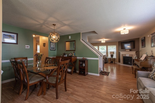 dining room with baseboards, a textured ceiling, wood finished floors, and a fireplace