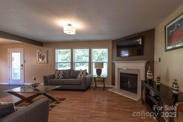 living area featuring dark wood-type flooring, a fireplace with flush hearth, plenty of natural light, and a textured ceiling