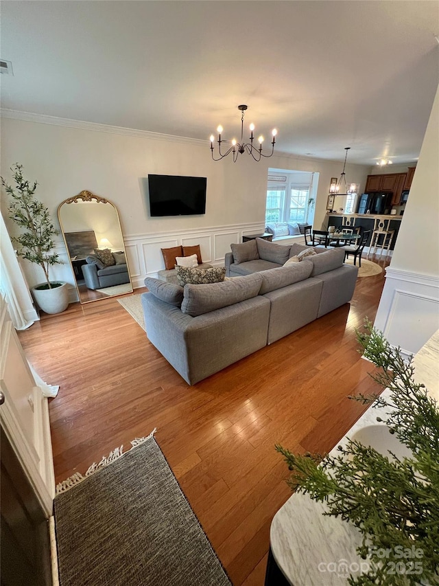 living area with wood finished floors, visible vents, an inviting chandelier, ornamental molding, and a decorative wall