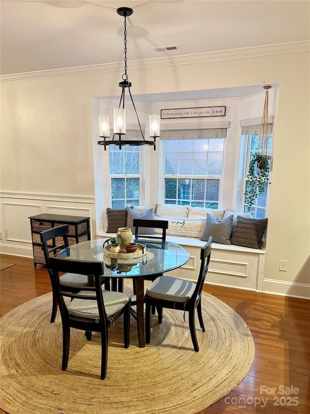 dining space featuring wood finished floors, a wainscoted wall, visible vents, crown molding, and a notable chandelier