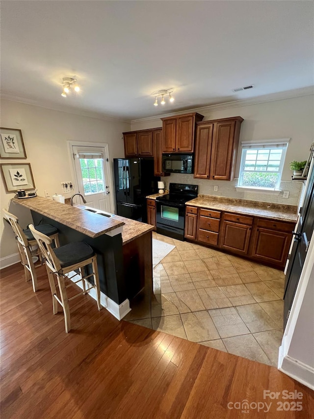 kitchen featuring plenty of natural light, black appliances, ornamental molding, and light wood finished floors