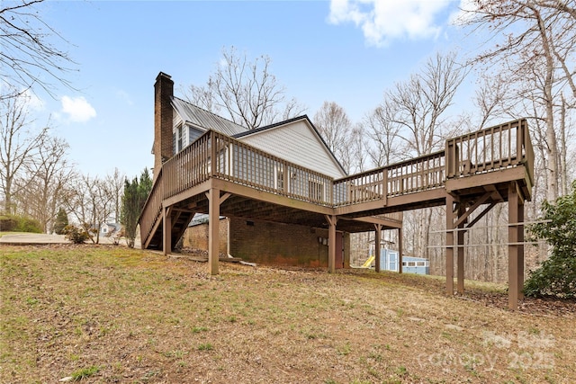 back of house with a wooden deck, stairs, a lawn, a chimney, and metal roof