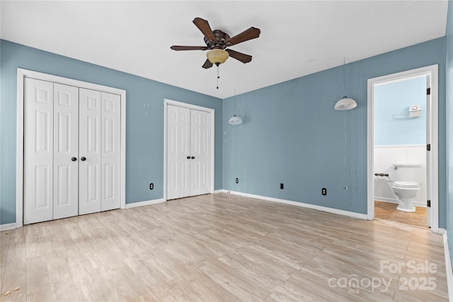 unfurnished bedroom with light wood-style flooring, baseboards, connected bathroom, and multiple closets