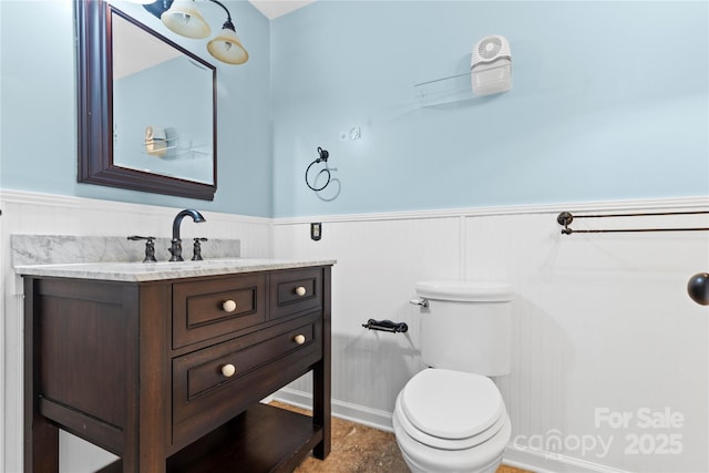 half bathroom with wainscoting, vanity, and toilet