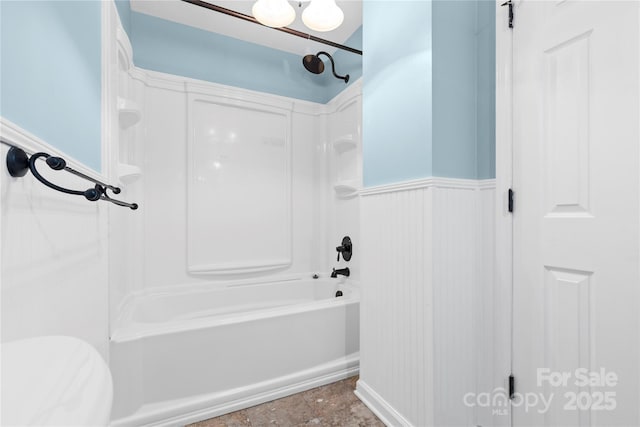 bathroom with bathing tub / shower combination, toilet, and a wainscoted wall