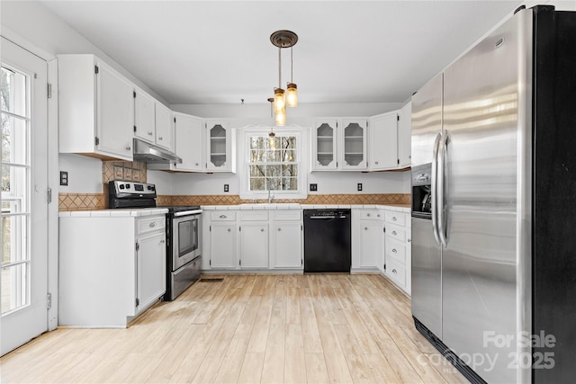 kitchen featuring light wood-style flooring, under cabinet range hood, white cabinetry, stainless steel appliances, and tile counters