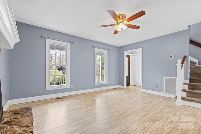 unfurnished living room featuring stairway, light wood-style floors, visible vents, and ceiling fan