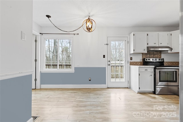 kitchen with stainless steel electric range oven, light wood finished floors, under cabinet range hood, white cabinetry, and a notable chandelier