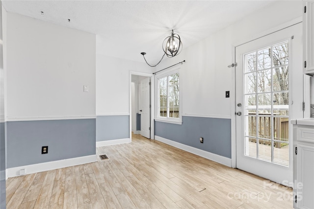 unfurnished dining area with a notable chandelier, light wood-style flooring, baseboards, and visible vents