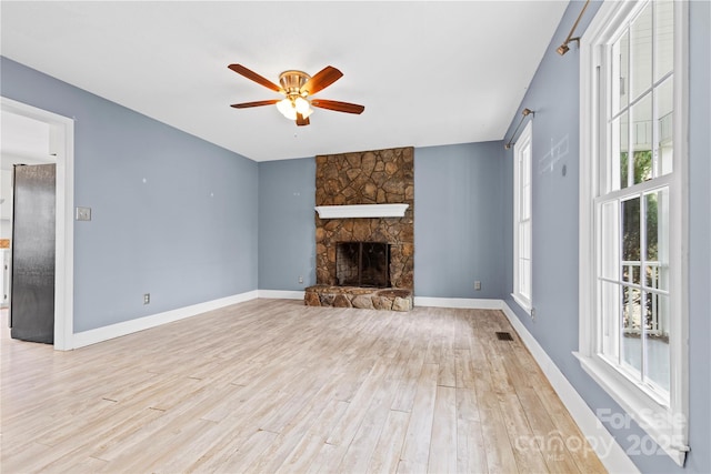 unfurnished living room featuring a stone fireplace, baseboards, light wood-type flooring, and ceiling fan