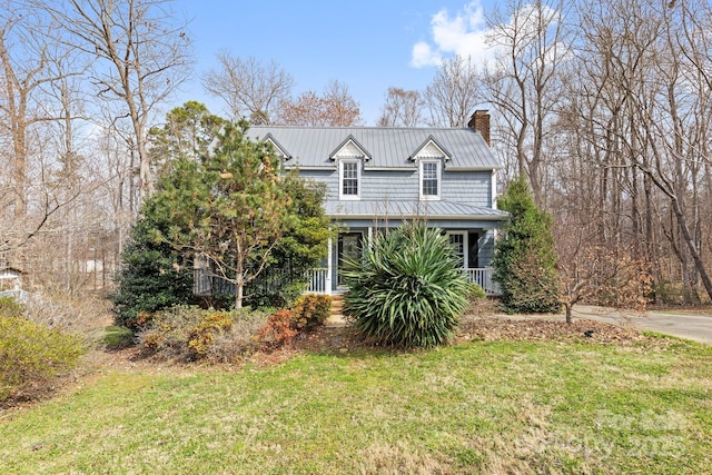 view of front of property with a standing seam roof, covered porch, a chimney, a front lawn, and metal roof