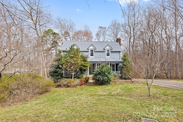 traditional-style home featuring a front lawn, a standing seam roof, a porch, metal roof, and a chimney