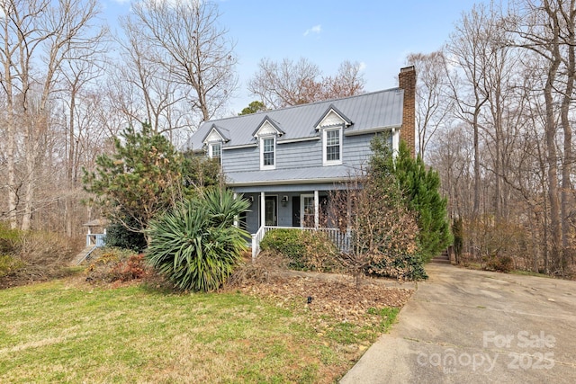 view of front facade with a porch, metal roof, a front yard, and a chimney