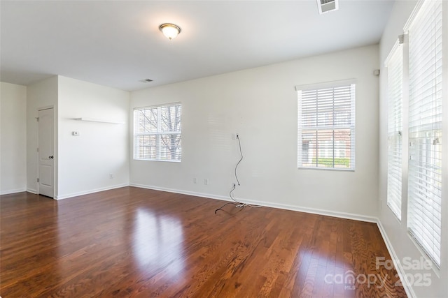 spare room with dark wood-style floors, visible vents, a wealth of natural light, and baseboards