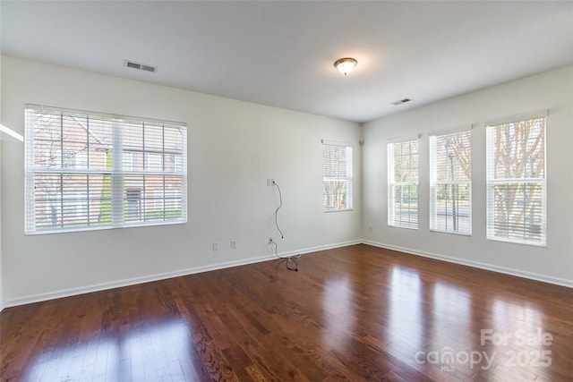 unfurnished room featuring visible vents, baseboards, a healthy amount of sunlight, and wood finished floors