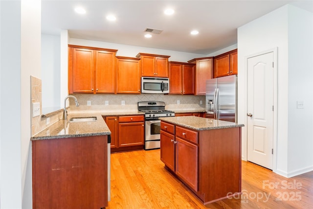 kitchen featuring visible vents, light stone counters, light wood-style flooring, stainless steel appliances, and a sink