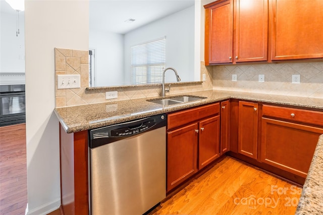 kitchen with tasteful backsplash, a sink, light wood-style flooring, and stainless steel dishwasher