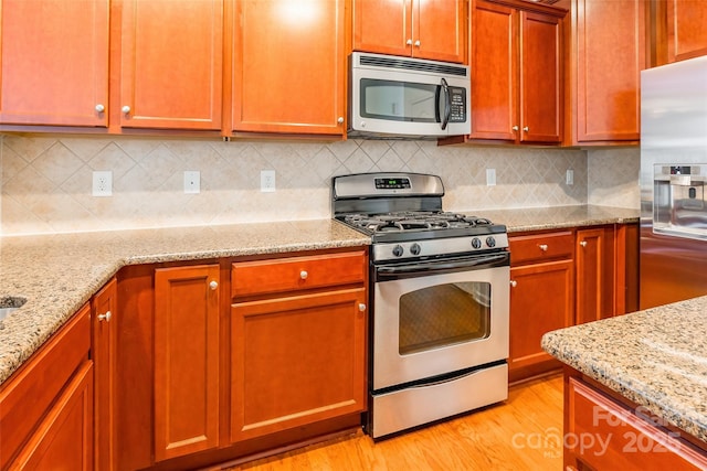 kitchen with tasteful backsplash, stainless steel appliances, light wood-type flooring, and light stone countertops