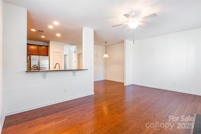 unfurnished living room with visible vents, dark wood-type flooring, a ceiling fan, a sink, and baseboards