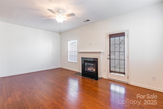 unfurnished living room with hardwood / wood-style floors, a ceiling fan, visible vents, and baseboards