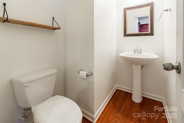 half bath with a sink, baseboards, toilet, and wood finished floors