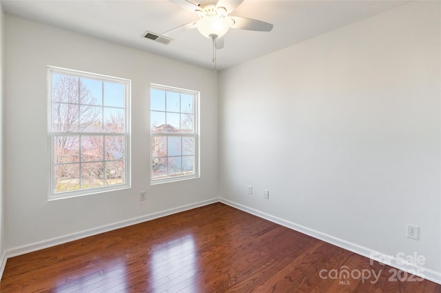 spare room with visible vents, a ceiling fan, dark wood-type flooring, and baseboards