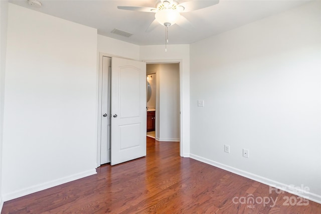 spare room with dark wood-type flooring, a ceiling fan, visible vents, and baseboards