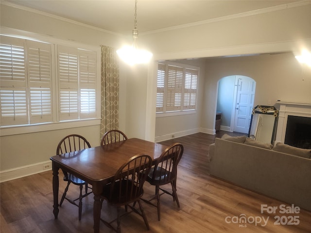 dining area with wood finished floors, baseboards, a fireplace, arched walkways, and crown molding