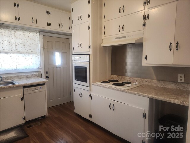 kitchen featuring visible vents, under cabinet range hood, light countertops, white appliances, and dark wood-style flooring