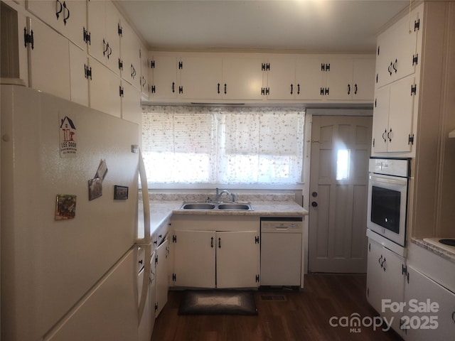 kitchen with a sink, white appliances, light countertops, and white cabinetry