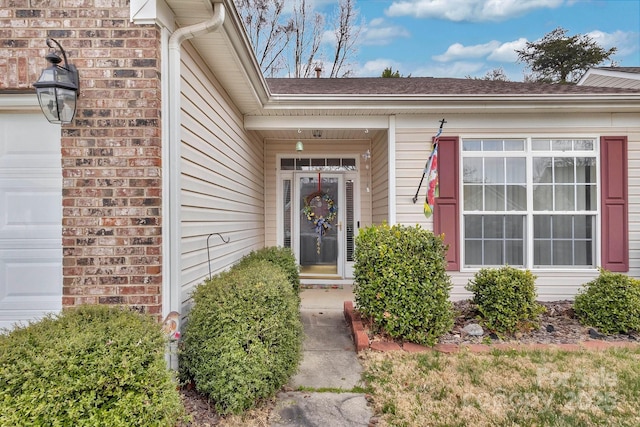 entrance to property with brick siding, an attached garage, and a shingled roof