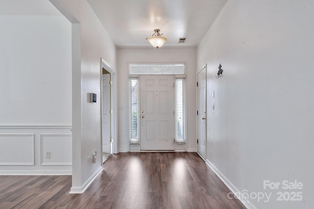 foyer entrance with visible vents, a decorative wall, and wood finished floors