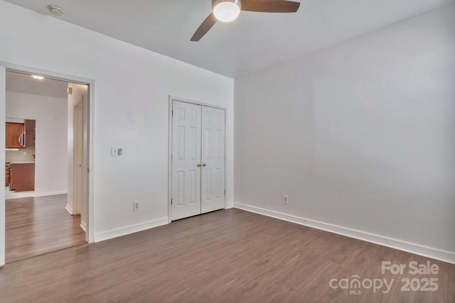 unfurnished bedroom with dark wood-type flooring, baseboards, a closet, and ceiling fan