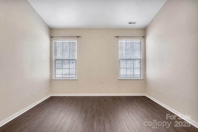 empty room with dark wood-style floors, visible vents, and baseboards