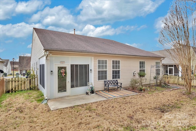 rear view of house with a lawn, roof with shingles, a patio, and fence