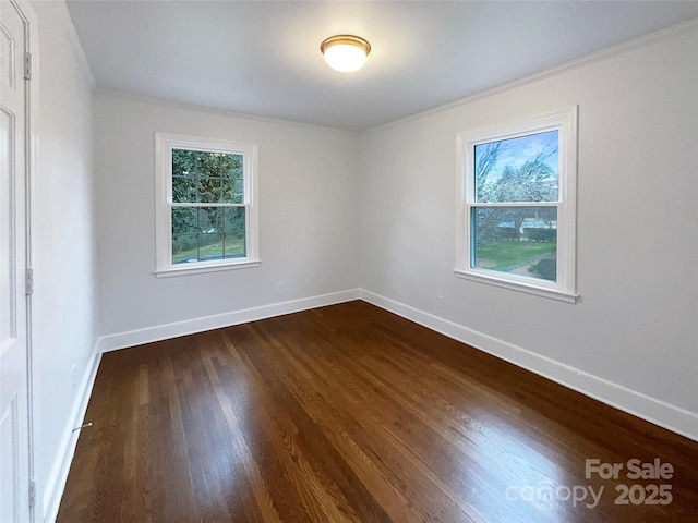 empty room featuring crown molding, baseboards, and dark wood-style flooring