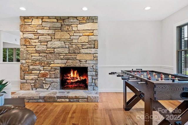 rec room with a stone fireplace, recessed lighting, wood finished floors, and a wealth of natural light