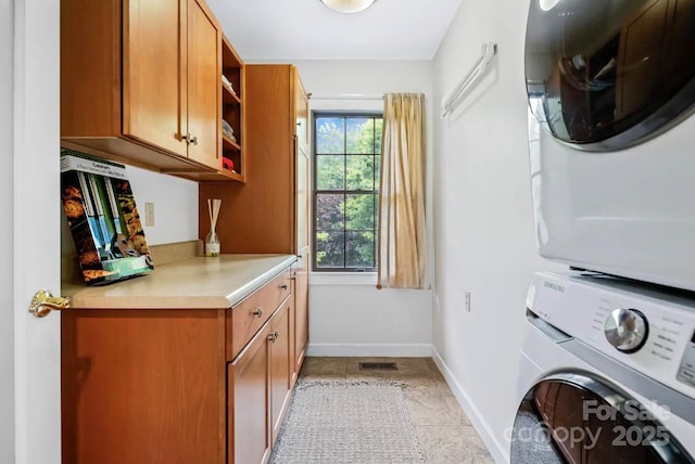 laundry room featuring visible vents, stacked washer / dryer, cabinet space, and baseboards