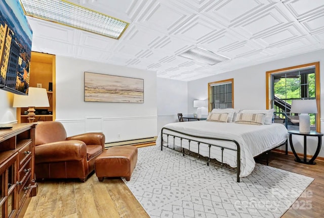 bedroom with an ornate ceiling, light wood-type flooring, and a baseboard heating unit