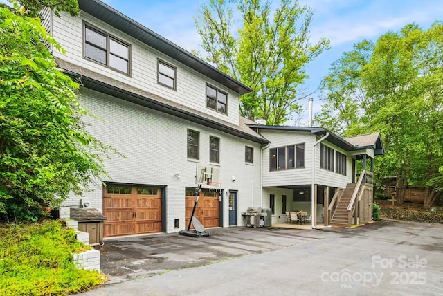 exterior space with stairway, brick siding, a garage, and aphalt driveway