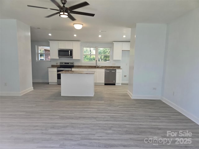 kitchen featuring baseboards, open floor plan, stainless steel appliances, white cabinetry, and a sink