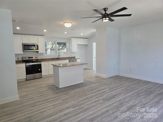 kitchen featuring a sink, a kitchen island, white cabinetry, stainless steel appliances, and light wood-style floors