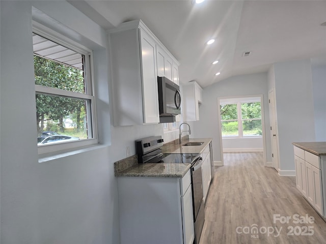 kitchen with visible vents, dark stone counters, white cabinets, stainless steel appliances, and a sink