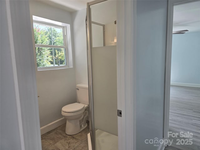 bathroom with baseboards, toilet, and a stall shower