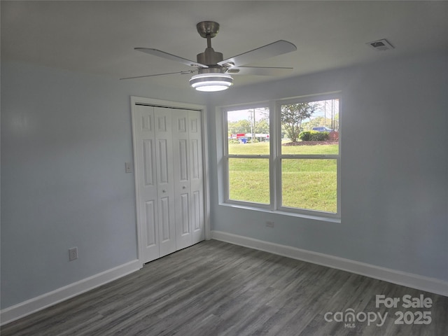 unfurnished bedroom with dark wood-style floors, visible vents, baseboards, ceiling fan, and a closet