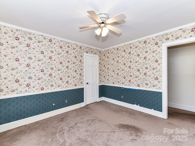 carpeted spare room with wallpapered walls, crown molding, and a ceiling fan