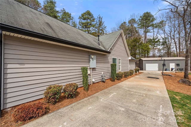 view of property exterior with a detached garage, an outdoor structure, and concrete driveway