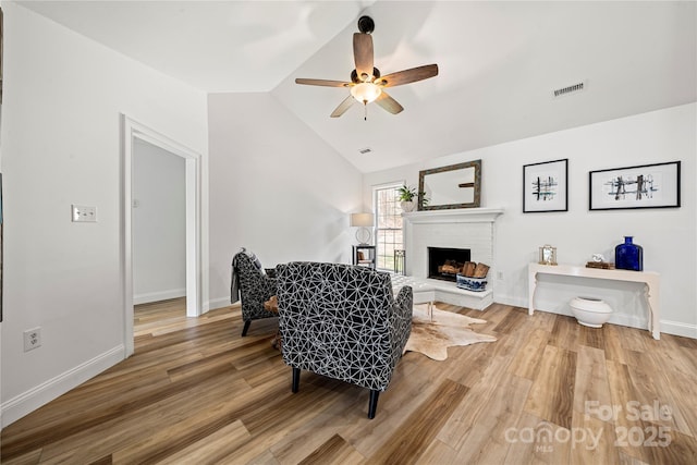 sitting room featuring a ceiling fan, visible vents, lofted ceiling, a brick fireplace, and light wood-type flooring