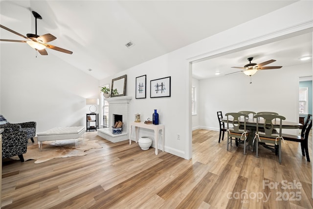 living area featuring a brick fireplace, light wood-style floors, and ceiling fan