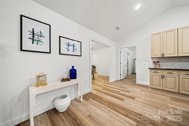 corridor featuring vaulted ceiling, baseboards, visible vents, and light wood-type flooring